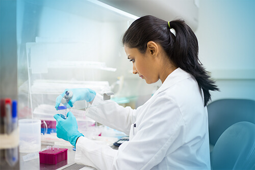woman in lab coat with surgical gloves testing items